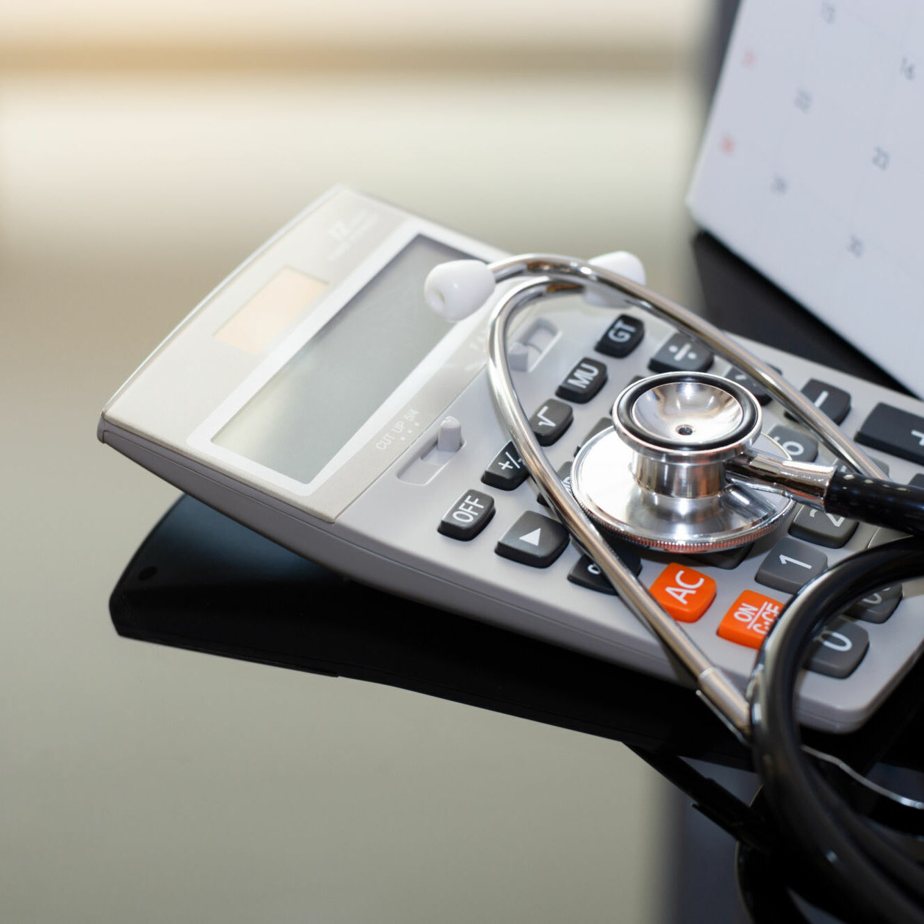 Healthcare costs and fees concept. Medical stethoscope with calculator and calendar isolated on dark table background.
